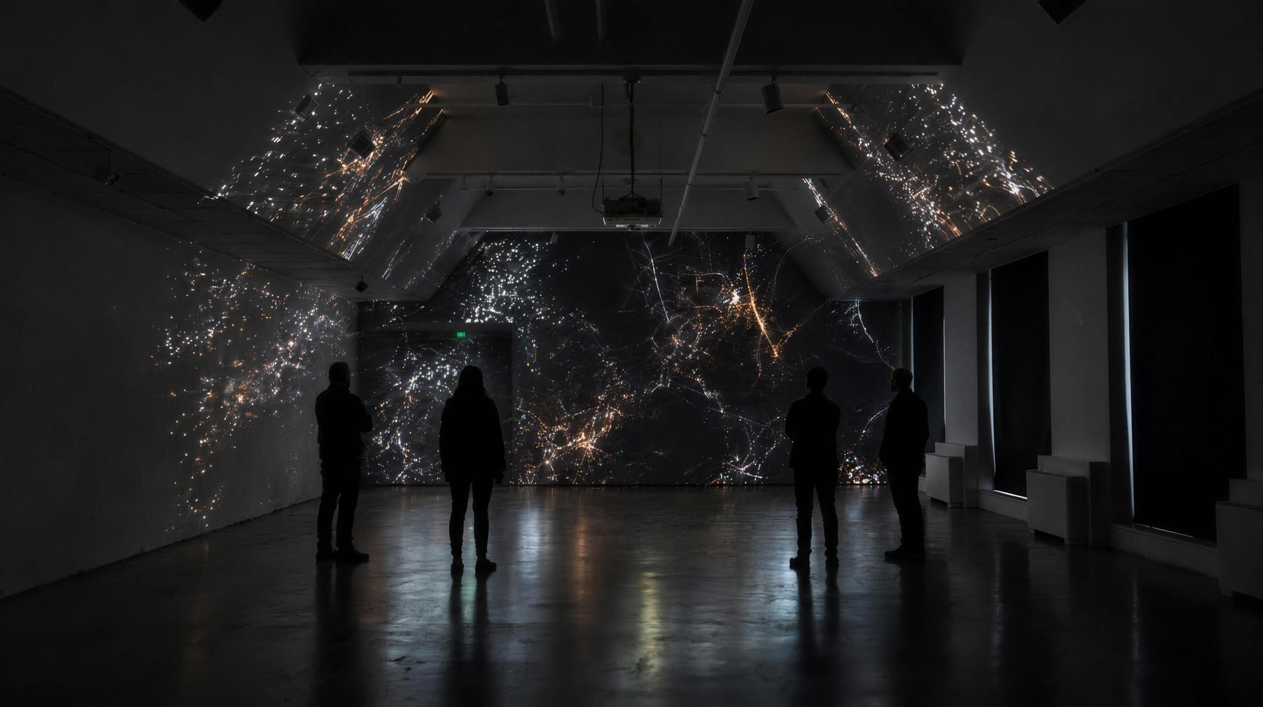 The far end wall mapped edge to edge with a concert visual, visitors watching in silhouette