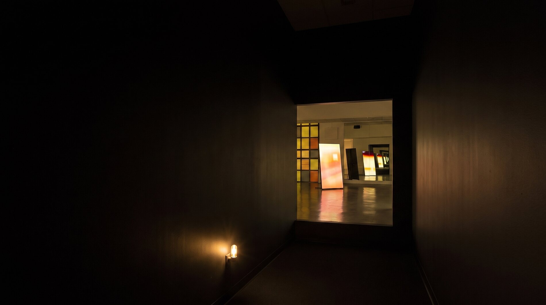 Looking out of the pitch black entry corridor into the lit gallery